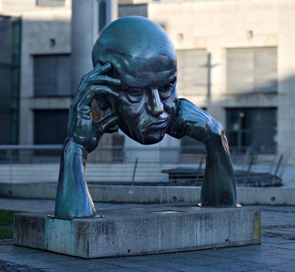 Bronze head sculpture of a man resting on his arms, displayed outdoors.